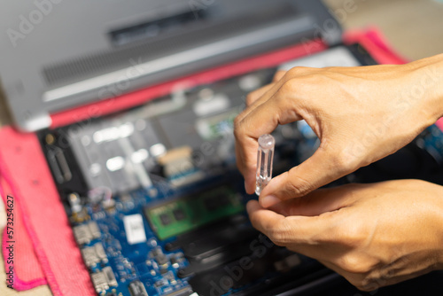 the hand is using a screwdriver to tighten the nut. To change the battery of a notebook computer by yourself. Changing electronic devices by yourself concept..