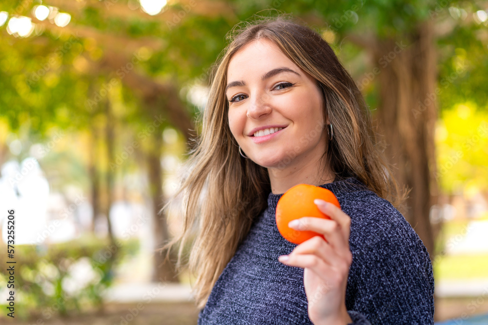 Young pretty Romanian woman holding an orange at outdoors smiling a lot Young pretty Romanian woman holding an orange at outdoors smiling a lot