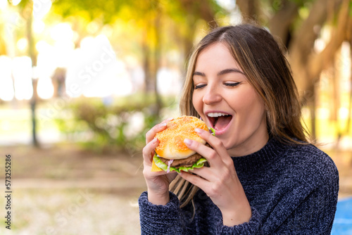 Young pretty Romanian woman holding a burger at outdoors
