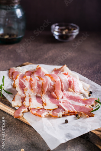 Raw smoked bacon and rosemary on a cutting board on the table. Hearty snack. Vertical view