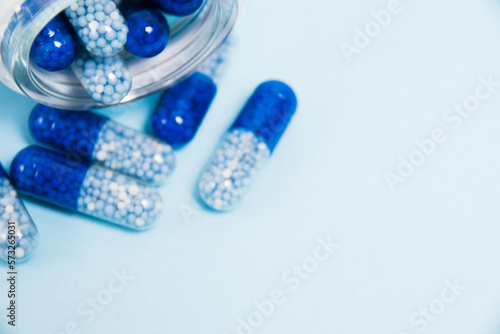 A transparent glass jar with vitamins in tablet form on a blue paper background