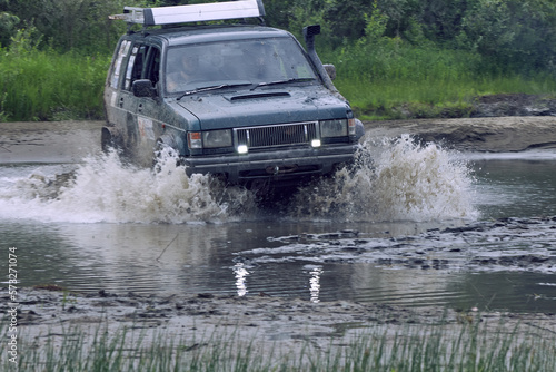 Off-road 4x4 car overcomes a ford at high speed, splashes from under the wheels when moving across the river. Extreme off-road tour in the forest.