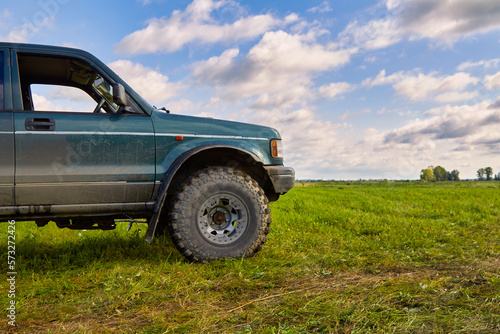 Close up 4x4 off-road car stands in a meadow against a beautiful blue sky with clouds. The concept of extreme travel, adventure or tourism in picturesque places