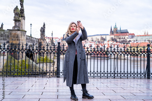 A girl with a backpack makes a photo on the phone of the Charles Bridge of Prague. Tourist girl takes pictures of Prague Castle. A woman holds a smartphone in her hands.
