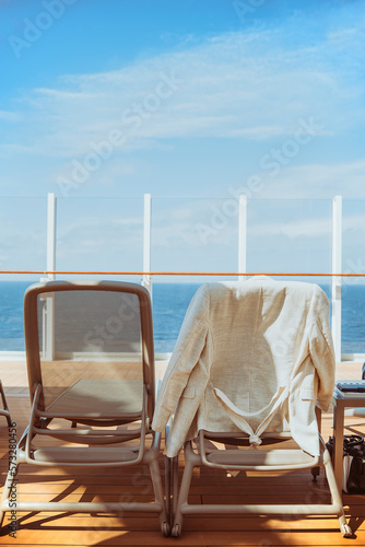 Empty lounge chairs on a deck of a cruise ship overlooking the blue sea.