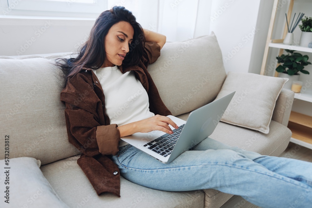 Woman freelancer on day off sitting on sofa with laptop at home online shopping on internet, smile Woman freelancer on day off sitting on sofa with laptop at home online shopping on internet, smile