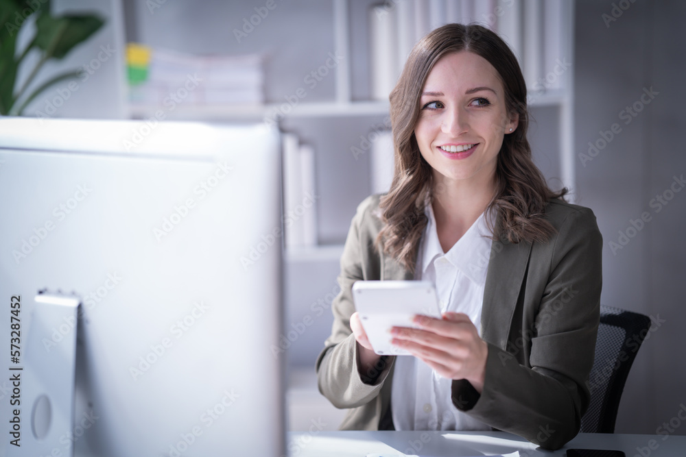 Sharing good business news. Attractive young businesswoman talking on the mobile phone and smiling while sitting at her working place in office and looking at laptop PC. Sharing good business news. Attractive young businesswoman talking on the mobile phone and smiling while sitting at her working place in office and looking at laptop PC.