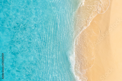 Summer seascape beautiful waves, blue sea water in sunny day. Top view from drone. Sea aerial view, amazing tropical nature background. Beautiful bright sea waves splashing and beach sand sunset light