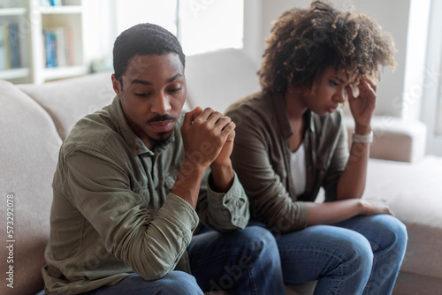Devastated black husband and wife sitting on sofa at home