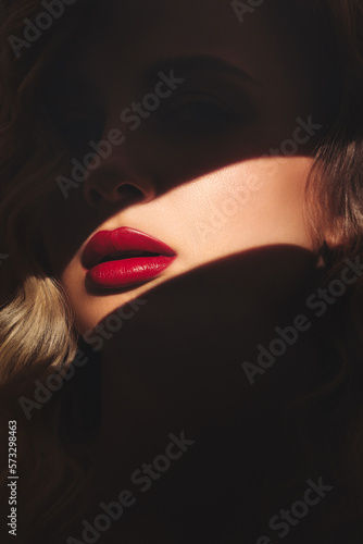 Bright red lips of a blonde woman highlighted by a streak of light.