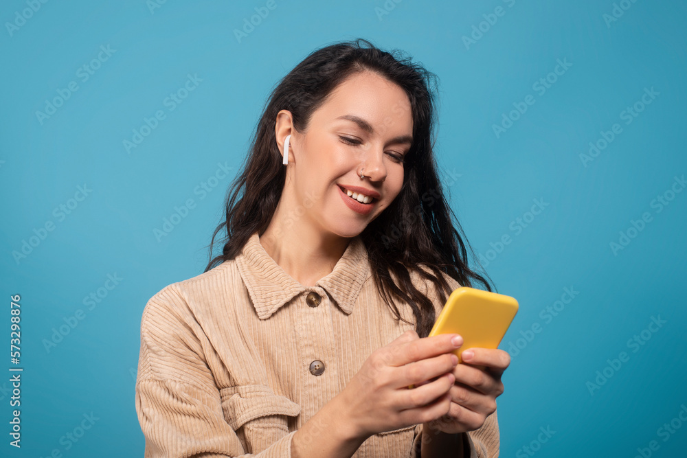 Cheerful millennial european female student in wireless headphones typing on phone, enjoy music, enjoy spare time Cheerful millennial european female student in wireless headphones typing on phone, enjoy music, enjoy spare time