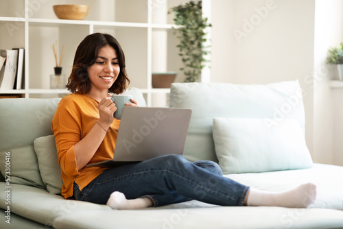 Domestic Pastime. Happy Arab Female Relaxing With Laptop And Coffee At Home
