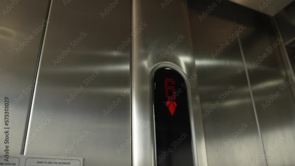 Digital LED red display with sixth floor number and direction arrows inside modern elevator with stainless steel metal cabin. Elevator rises, shadows of rungs and opening doors appear on walls. Digital LED red display with sixth floor number and direction arrows inside modern elevator with stainless steel metal cabin. Elevator rises, shadows of rungs and opening doors appear on walls.
