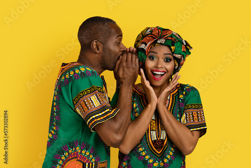 Black man sharing secrets with girlfriend, african couple on yellow