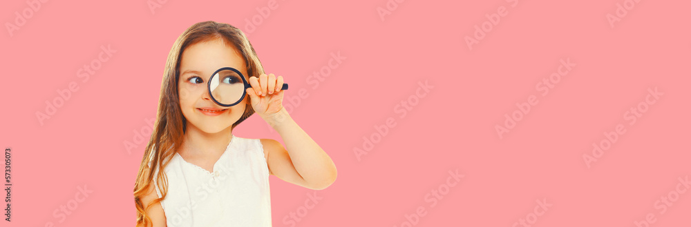 Portrait of child looking through magnifying glass looking away on pink background, blank copy space for advertising text Portrait of child looking through magnifying glass looking away on pink background, blank copy space for advertising text