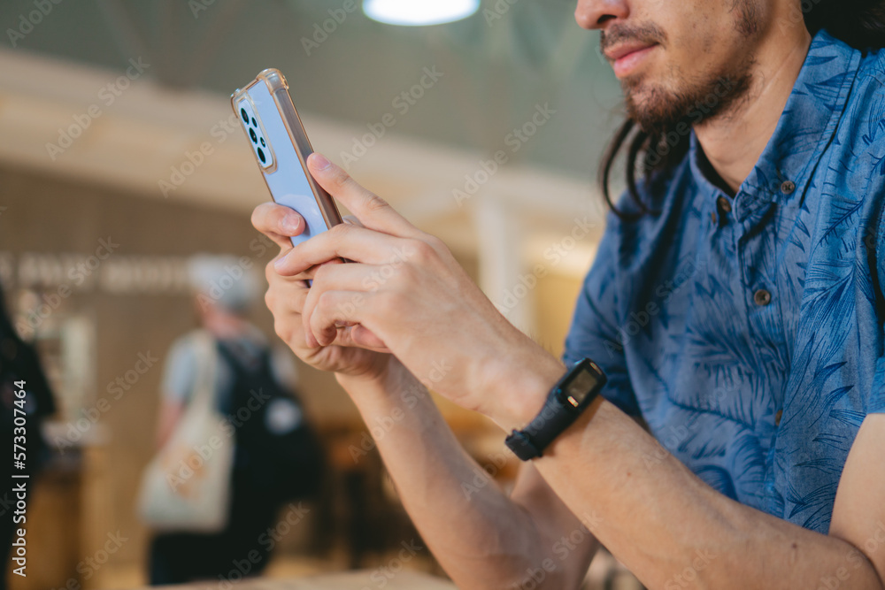 Young Latin man wearing a smart watch and texting on his smart phone in a public place.