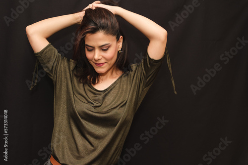 Portrait of smiling woman in green blouse with her hands on her head looking down. 