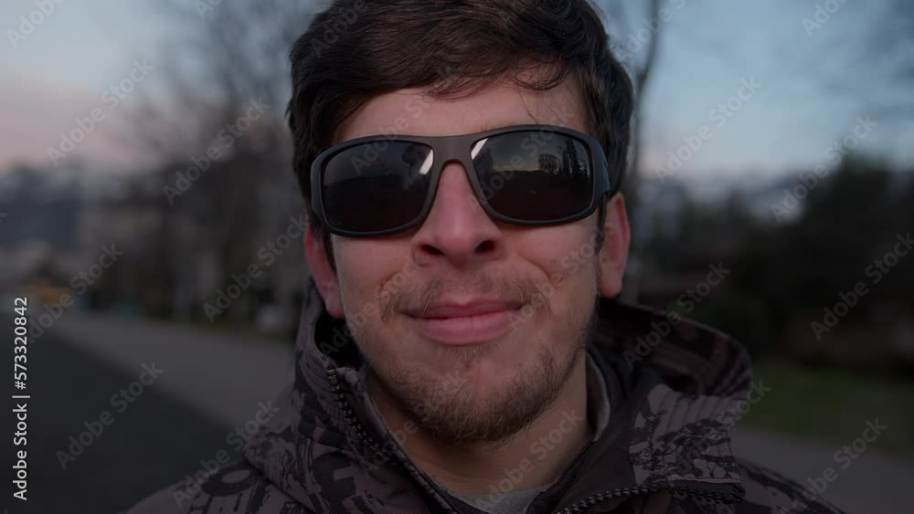 A Handsome Young Man in Sunglasses Smiling at the Camera Outdoors in a Stylish Coat A Handsome Young Man in Sunglasses Smiling at the Camera Outdoors in a Stylish Coat