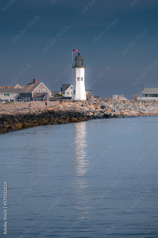 White lighthouse, with reflection, along the New England coastline.