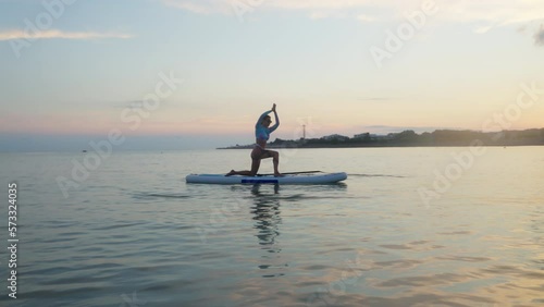 Girl practicing yoga on paddleboard at sunset