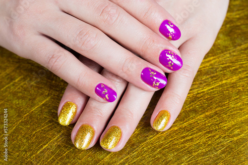 Female hands with a gold and purple colour nails. Nail design. Artistic manicure with gel polish