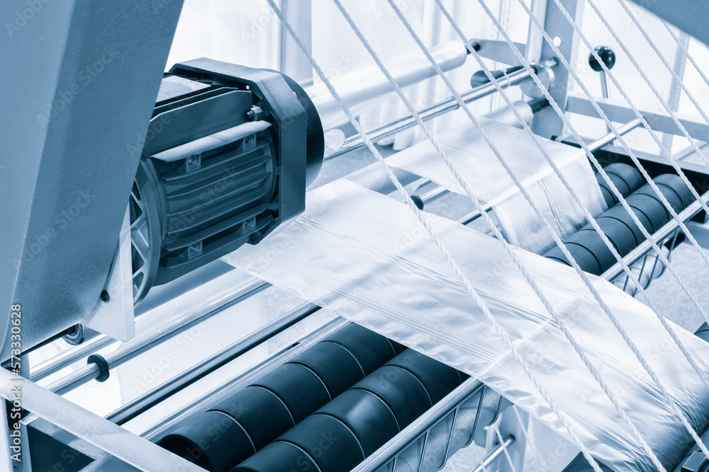Fototapeta premium Automatic polyethylene plastic bag production machine with lighting effect. Close-up of the roller of the plastic bag production machine in the light blue scene. product packaging concept