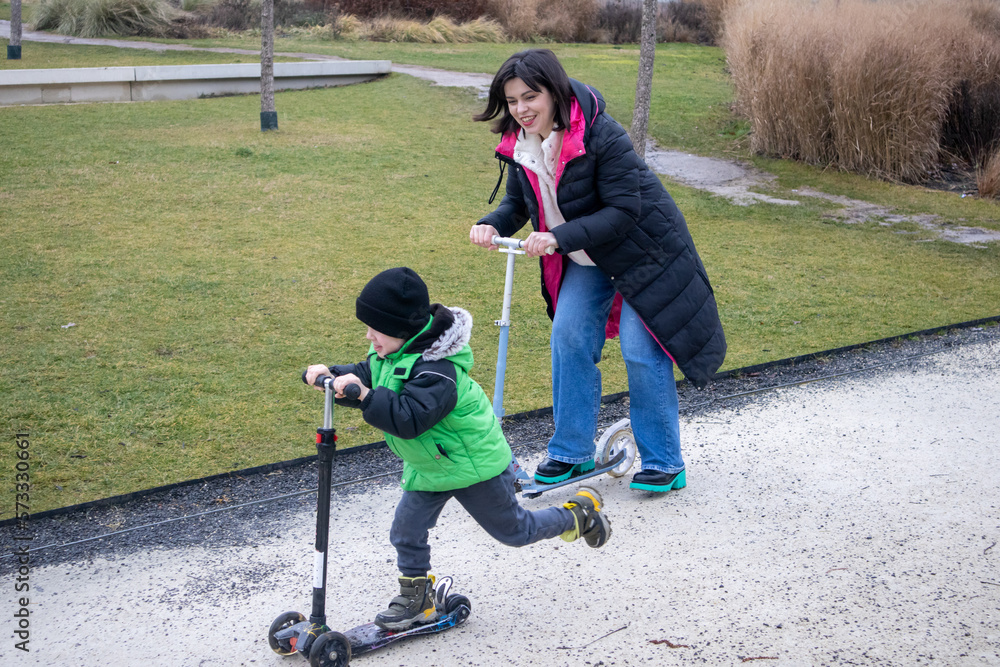 Fototapeta premium A mother and her son learn to ride a scooter in the park