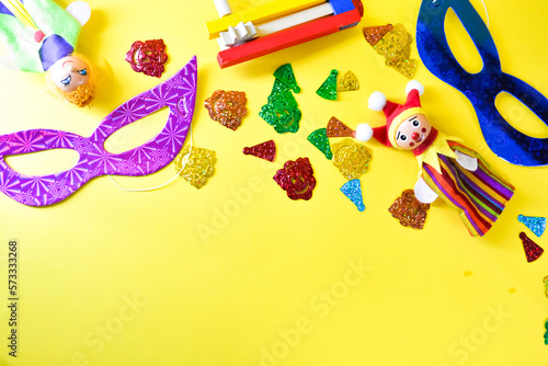 Carnival party background with carnival mask and clown hat. Birthday celebration concept. Top view with copy space carnival, party and Purim celebration concept (jewish carnival holiday) over yellow 