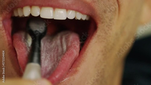 Close up of man brushing his tongue with a manual toothbrush
