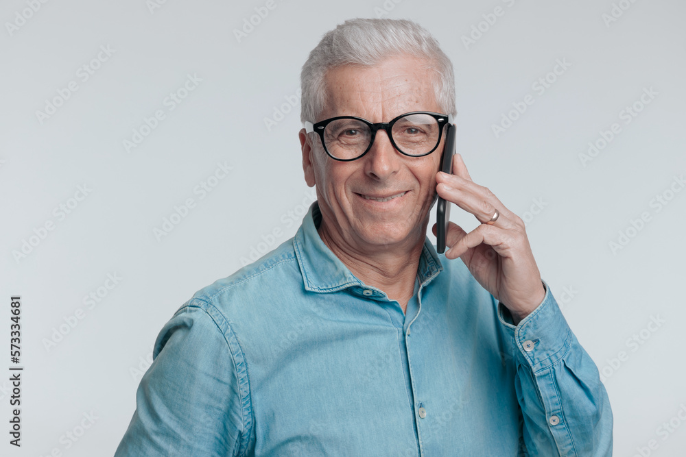 portrait of casual man in his 60s talking on the phone and smiling portrait of casual man in his 60s talking on the phone and smiling