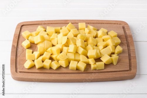Wooden board with fresh diced potatoes on a light gray background. Stage of cooking vegetable stew