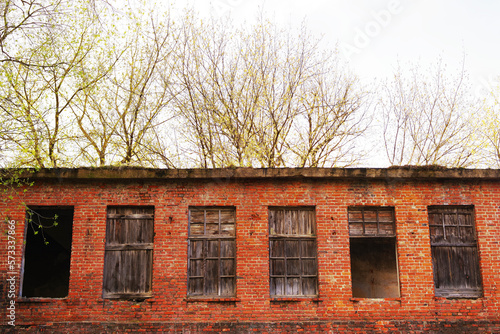 Wall of an old red brick house with empty and boarded up windows. Abandoned building, unfinished