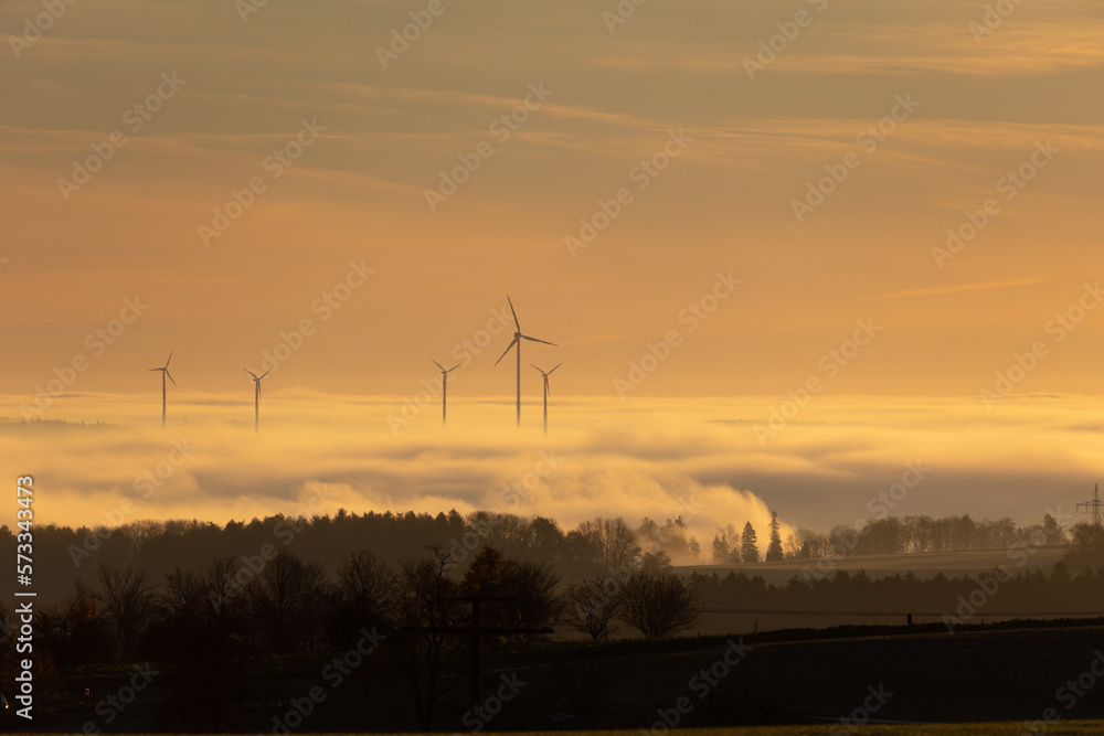 silhouette of some wind turbines standing out above a low layer of clouds. Pastel coloured sky. silhouette of some wind turbines standing out above a low layer of clouds. Pastel coloured sky.