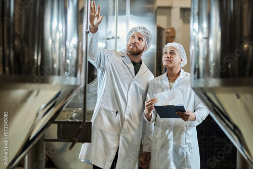 Fotografia Two workers wearing lab coats inspecting equipment at food factory