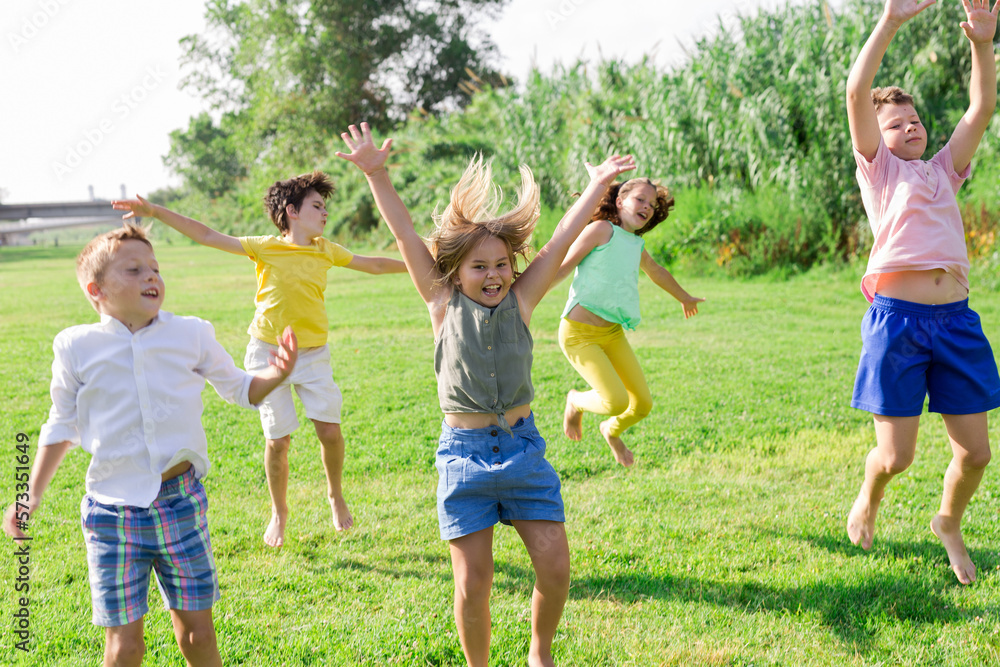 Portrait of cheerful preteen girls and boys jumping together in summer city park. Concept of happy childhood..