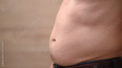 Man hits himself on stomach and takes folds of fat on his stomach, excess weight. photo