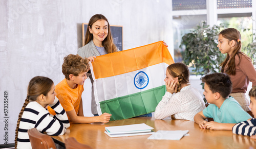 Decent teacher showing India flag to group of preteen schoolchildren in classroom during lesson