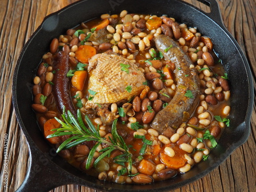 French Cassoulet, a meat and beans stew, in a cast iron skillet, on a rustic wooden table