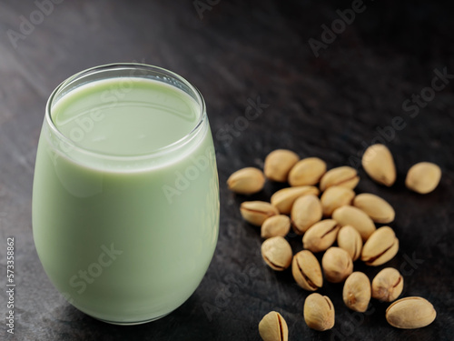 Organic pistachio milk in glass and pistachios on a dark green background. Non dairy alternative milk. Copy space