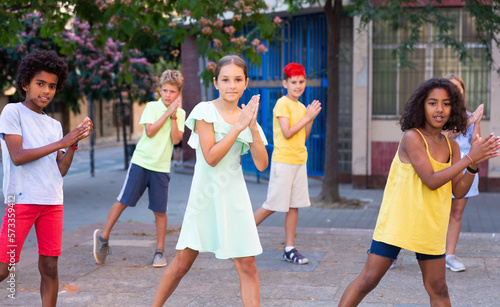 Group of modern cheerful tweenagers performing street dance choreography outdoors in summer..