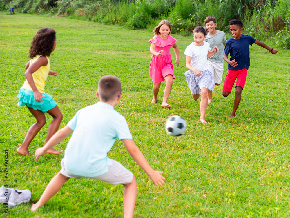 Obraz premium International group of active tweenagers having fun together outdoors, playing football on green grass in summertime