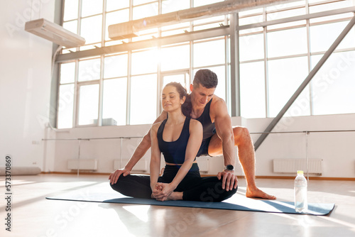 athletic couple in sportswear on mats doing yoga  man yoga trainer helps woman to warm up  yoga instructor teaches girl