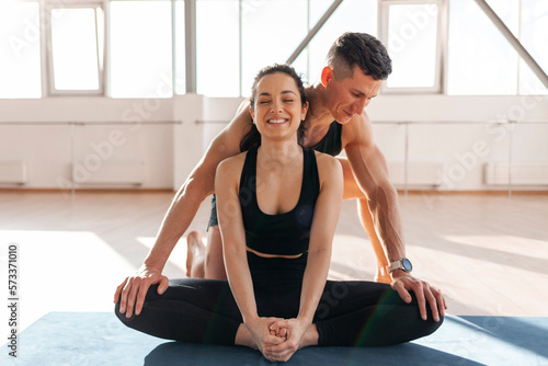 athletic couple in sportswear on mats doing yoga, man yoga trainer helps woman to warm up, yoga instructor teaches girl
