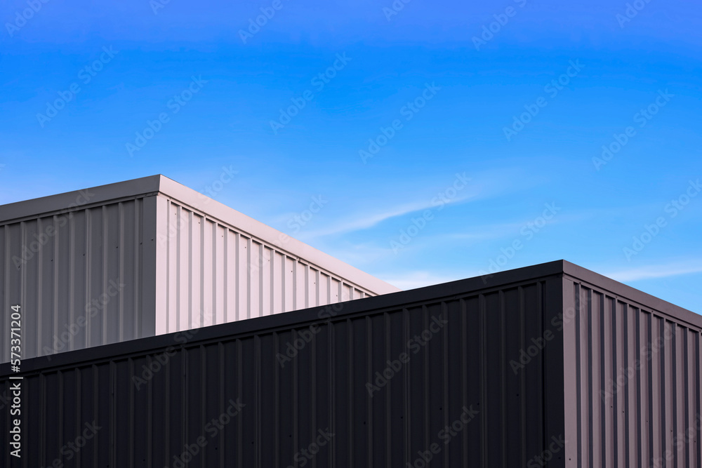 High section of 2 black and white corrugated metal Factory Buildings against blue sky background High section of 2 black and white corrugated metal Factory Buildings against blue sky background