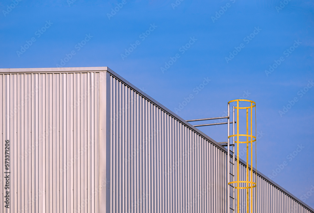 Corrugated iron Industrial Building Wall with cylinder Ladder against blue sky Background, perspective side view with copy space Corrugated iron Industrial Building Wall with cylinder Ladder against blue sky Background, perspective side view with copy space