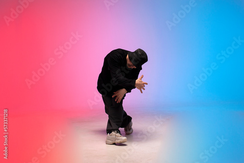 dancer dances hip hop in neon lighting, young guy moves his arms to the side and dances breakdance