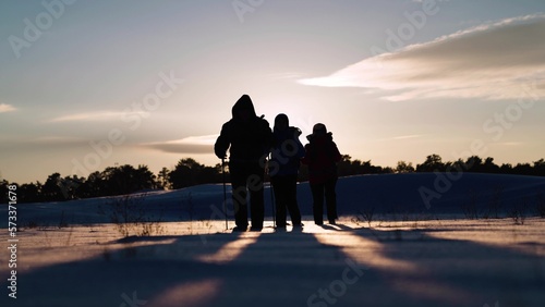 Group of successful hikers walking through snow towards success and adventure. Tourists with backpacks travel through snowy valley in rays of sunset to forest. Business partners, Teamwork of business.