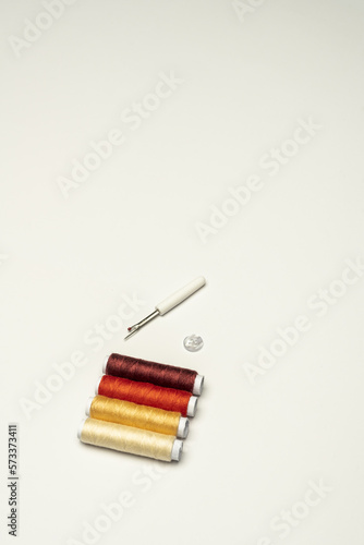 A few spools of colored sewing threads on a plain white background with a needle and a button