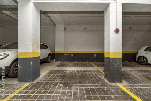 Parking spaces delimited with yellow paint on the ground floor of a building with a garage and parked vehicles
