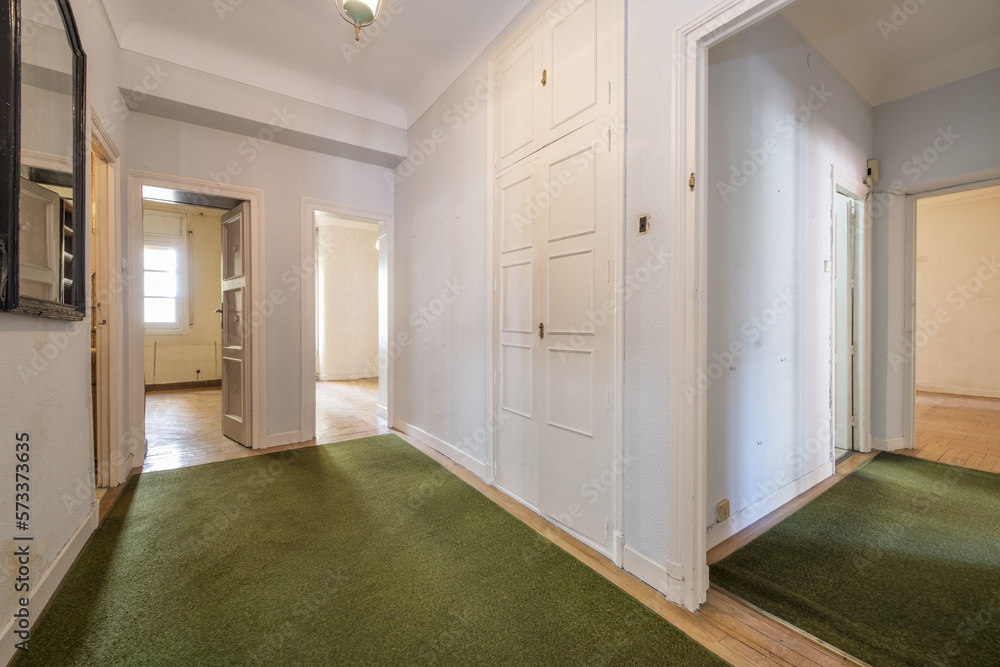 Distributor space of a house with wooden floors covered with green carpets, a built-in wardrobe and wooden access doors to empty rooms Distributor space of a house with wooden floors covered with green carpets, a built-in wardrobe and wooden access doors to empty rooms